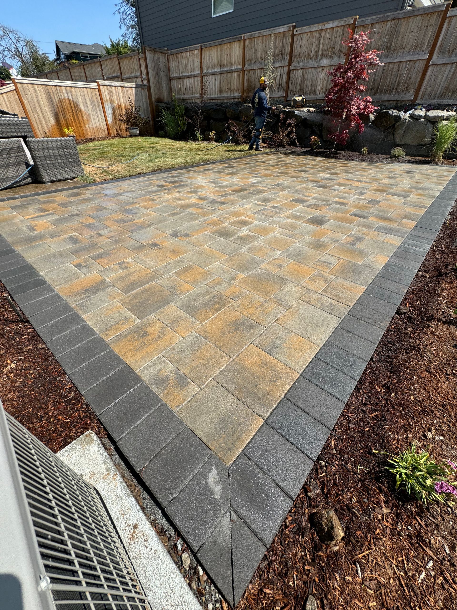 A man is standing in the middle of a patio in a backyard.