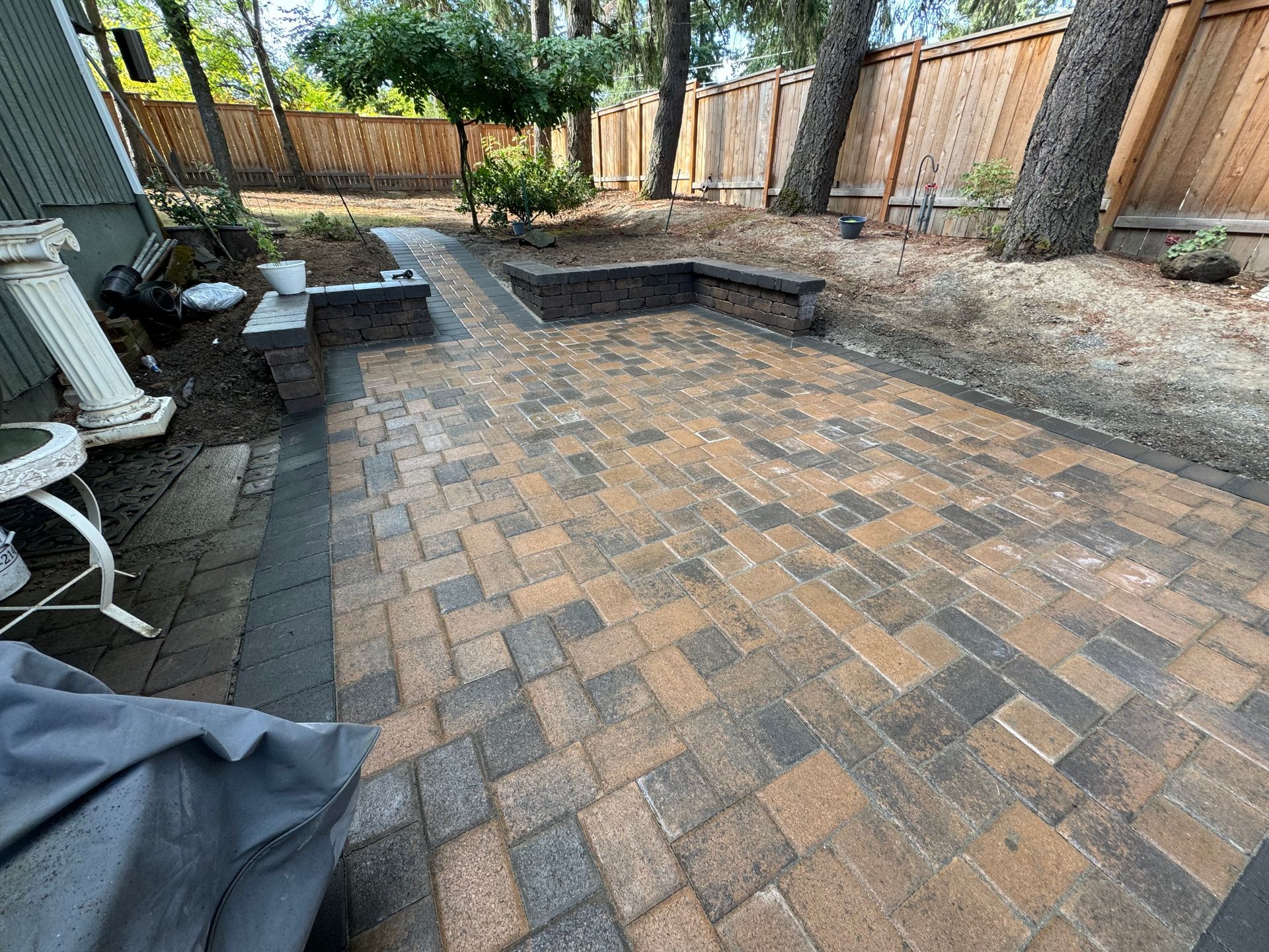 A brick patio in a backyard with a wooden fence in the background.