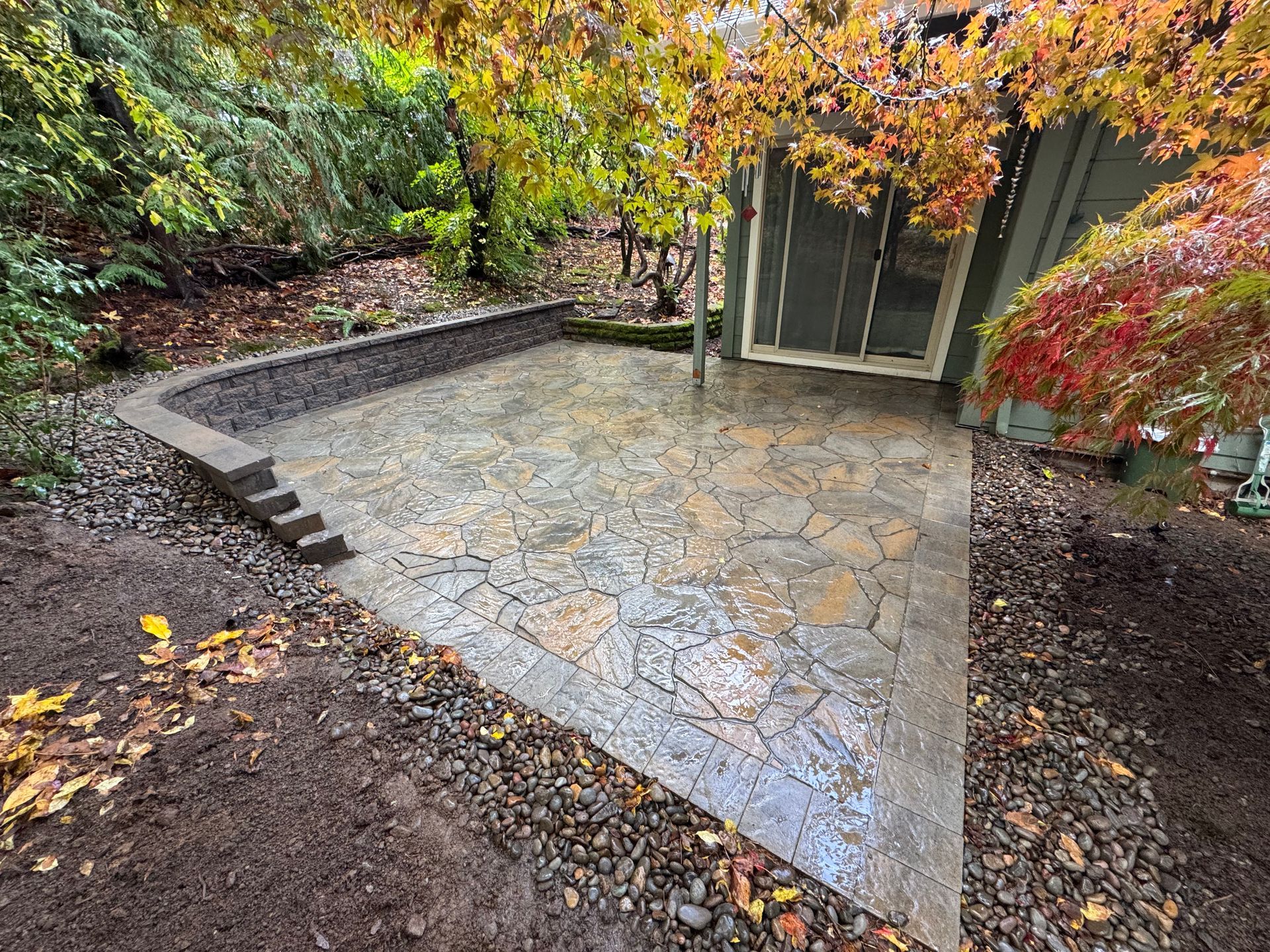 A stone patio in a backyard next to a green shed.