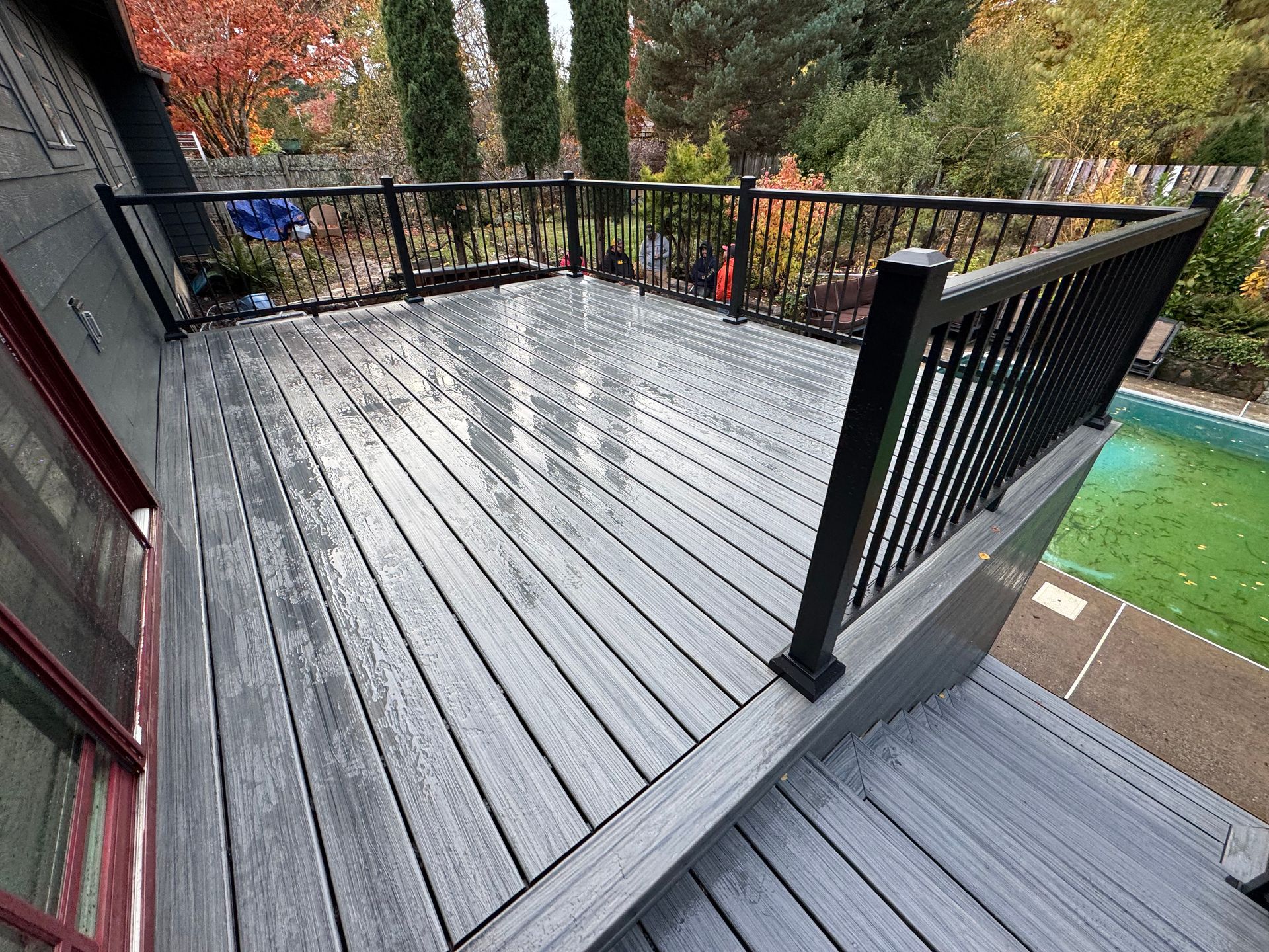 A large wooden deck with a black railing and stairs leading up to it.