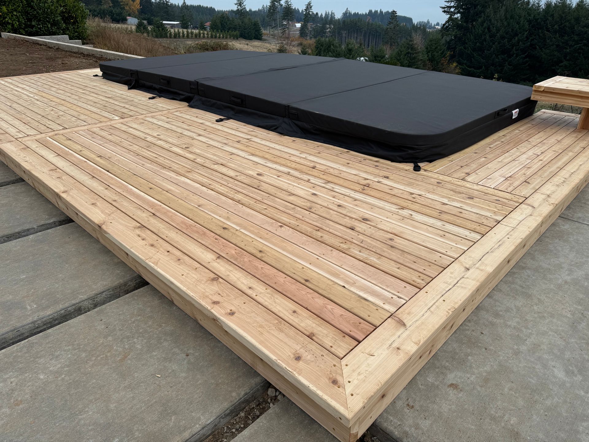 Wooden deck with a covered hot tub, outdoors on a concrete patio.