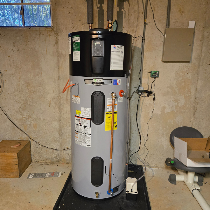Water heater tank in a basement utility room, with pipes, labels, and a concrete floor.