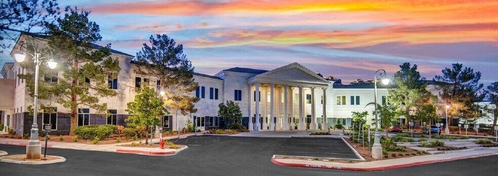 Dusk view of a lit white building with columns, trees, and a colorful sunset sky over an empty parking lot