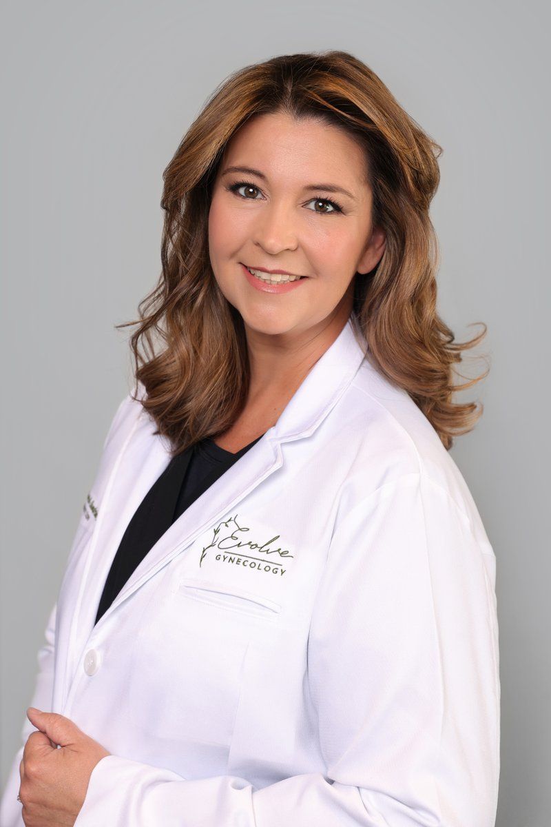 Healthcare professional in a white lab coat smiling against a gray background