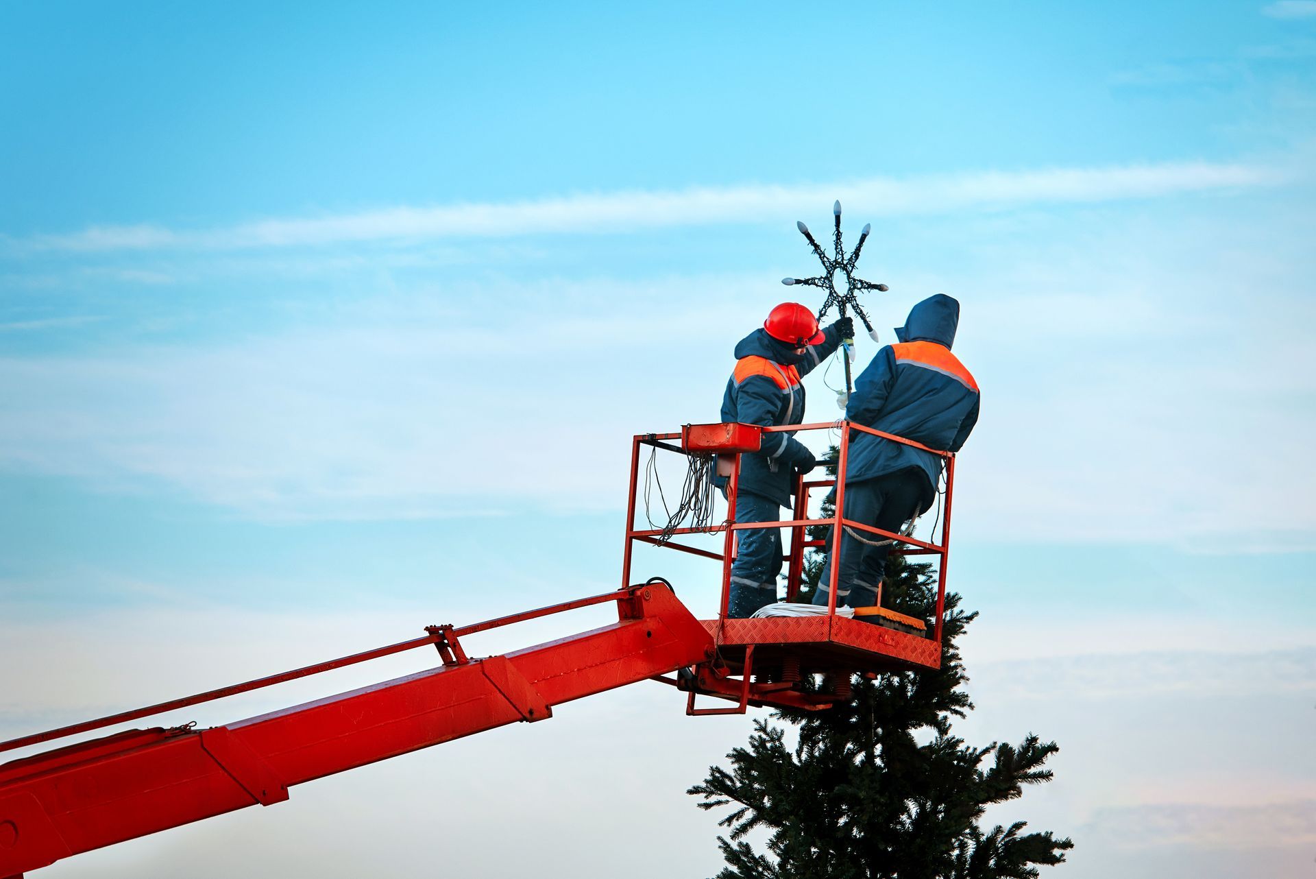Two workers install a treetop star using equipment from reliable crane rental services.