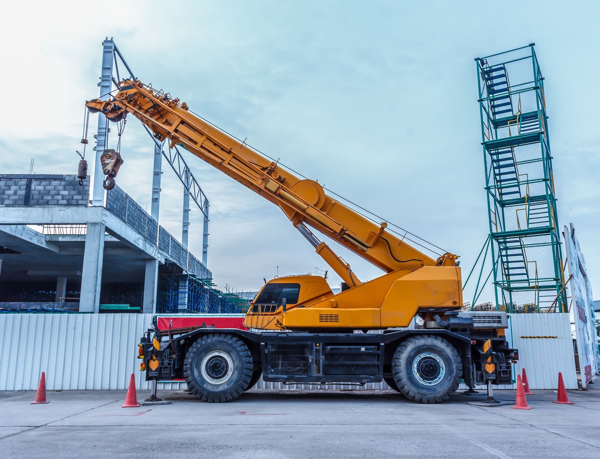 Yellow mobile crane lifting metal trusses near building frame. Yellow mobile crane lifting metal trusses near building frame.