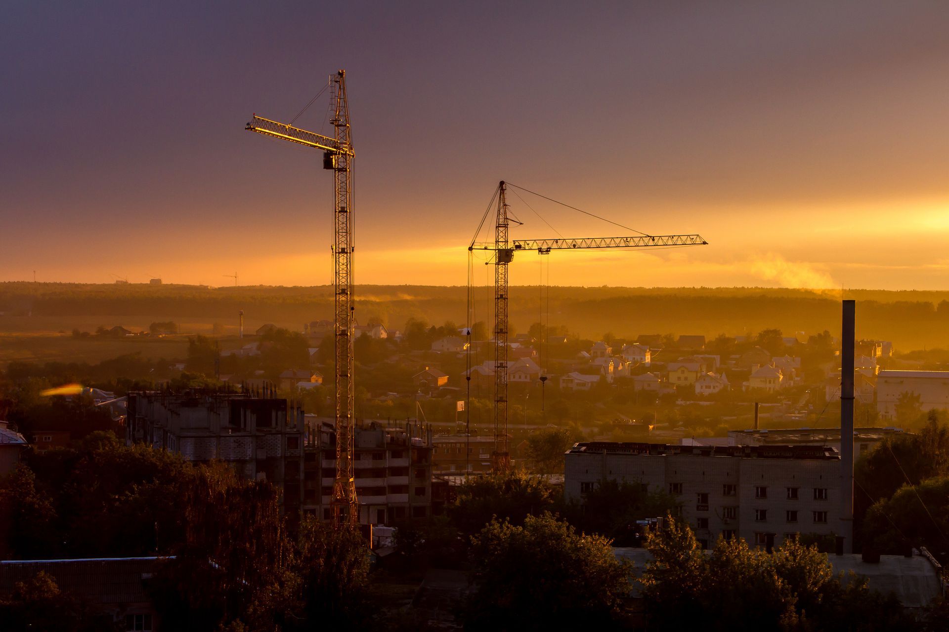 Industrial landscape at dusk, with two construction cranes between the buildings.