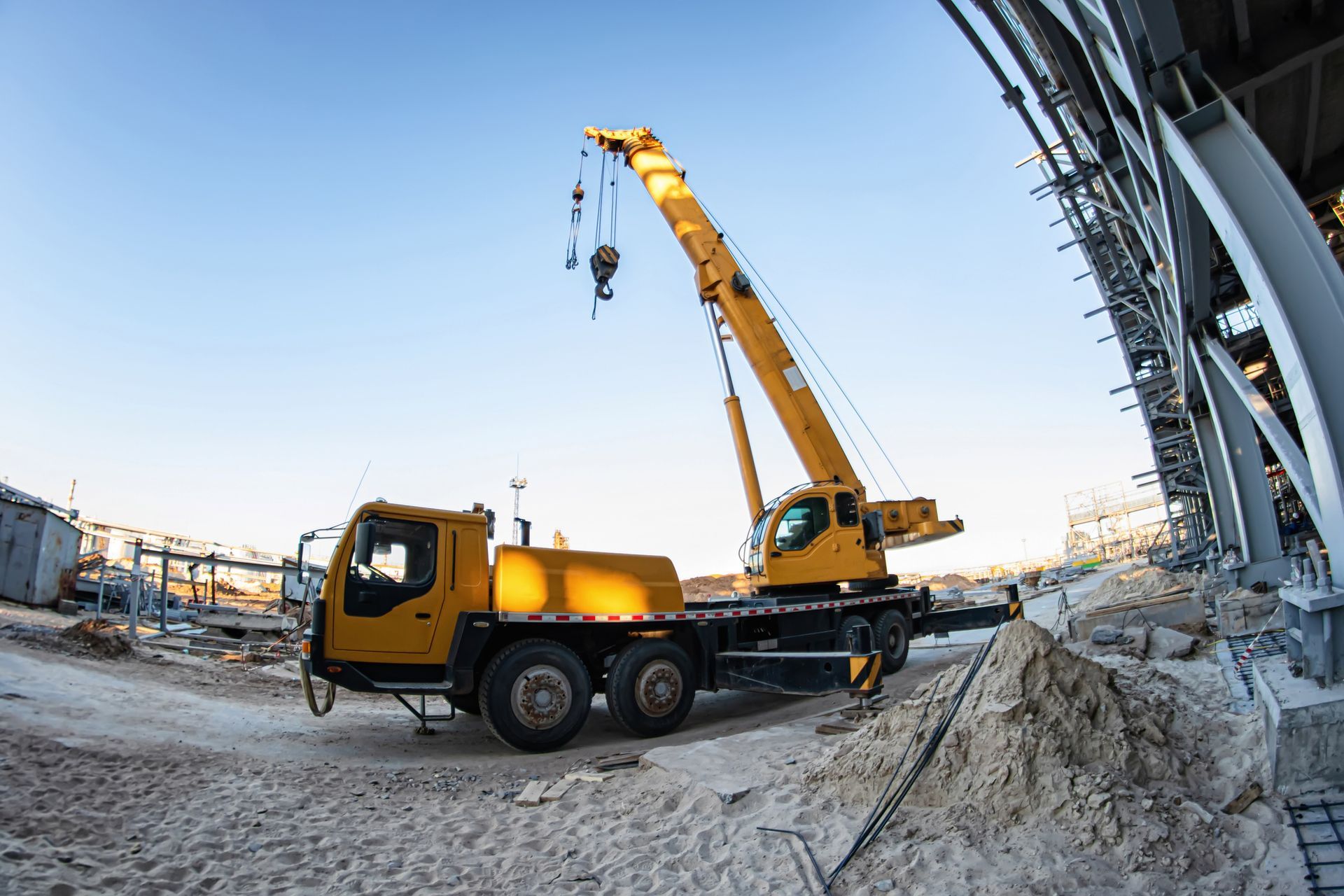 Image of a yellow crane truck parked at construction site under blue sky. Image of a yellow crane truck parked at construction site under blue sky.