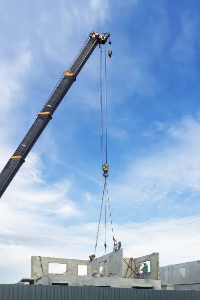 Construction site with a crane lifting a concrete wall against the clear blue sky.