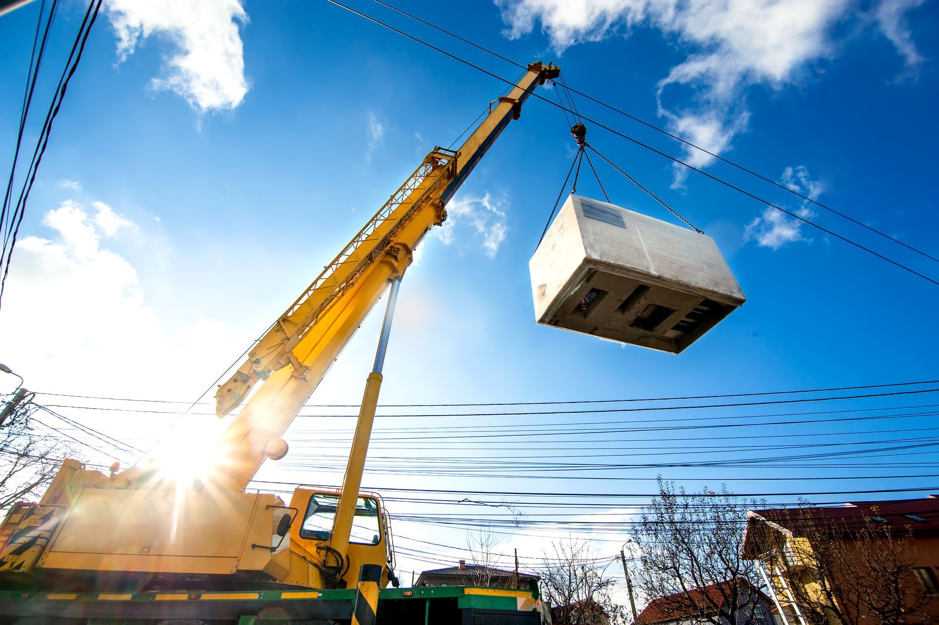 A yellow crane operating by lifting and moving an electric generator, showcasing crane rental.