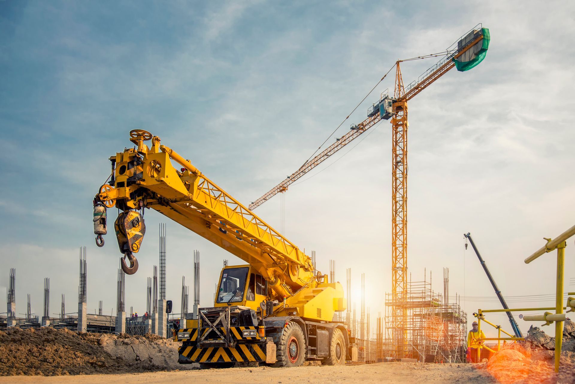 Image of a mobile crane on a road and a tower crane in a construction.