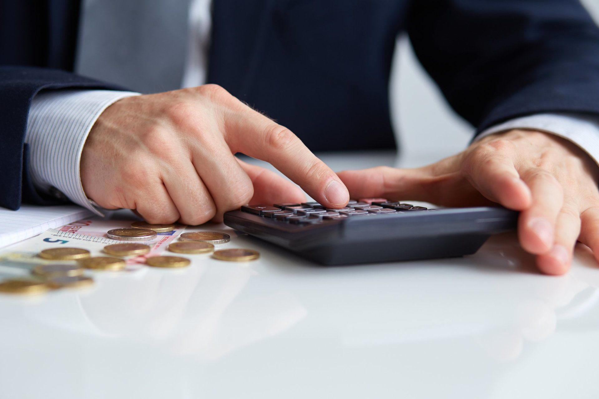 A man is using a calculator with coins on the table.