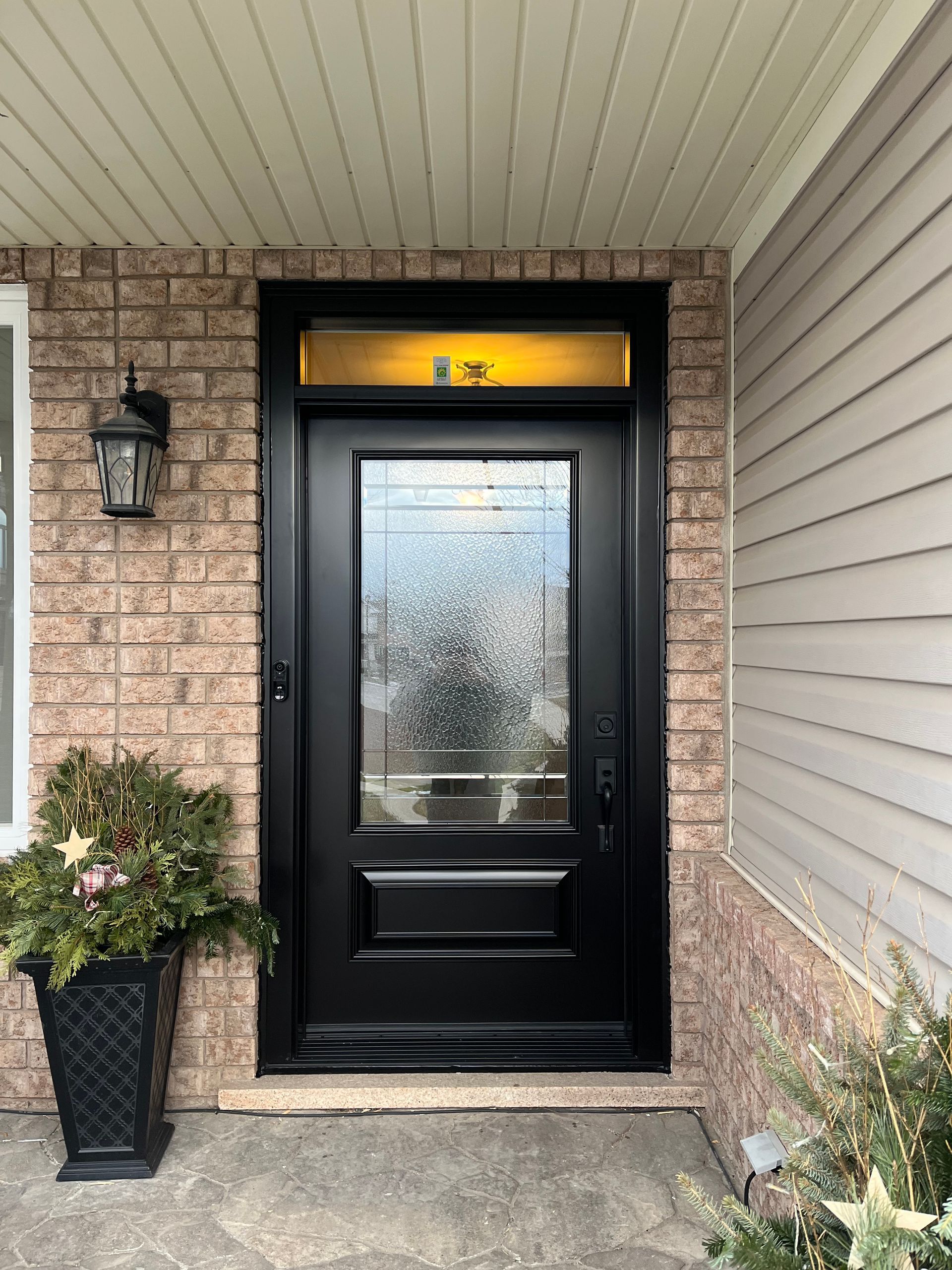 The front door of a brick house with a black door and a potted plant in front of it.