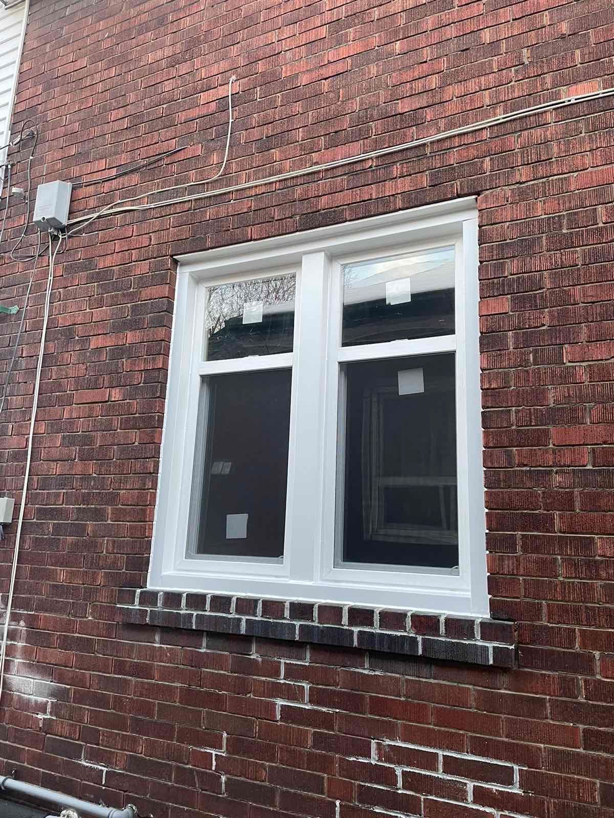 A white window is on the side of a brick building.