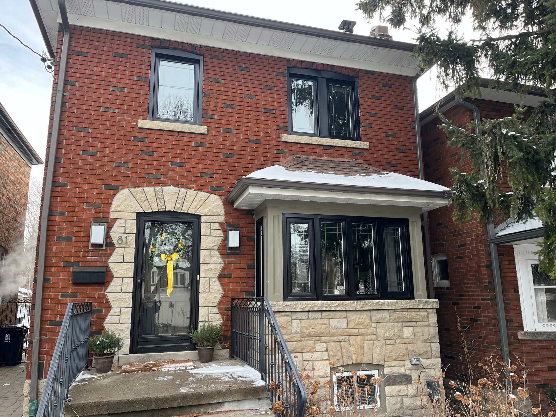 A red brick house with black windows and a yellow bow on the front door.
