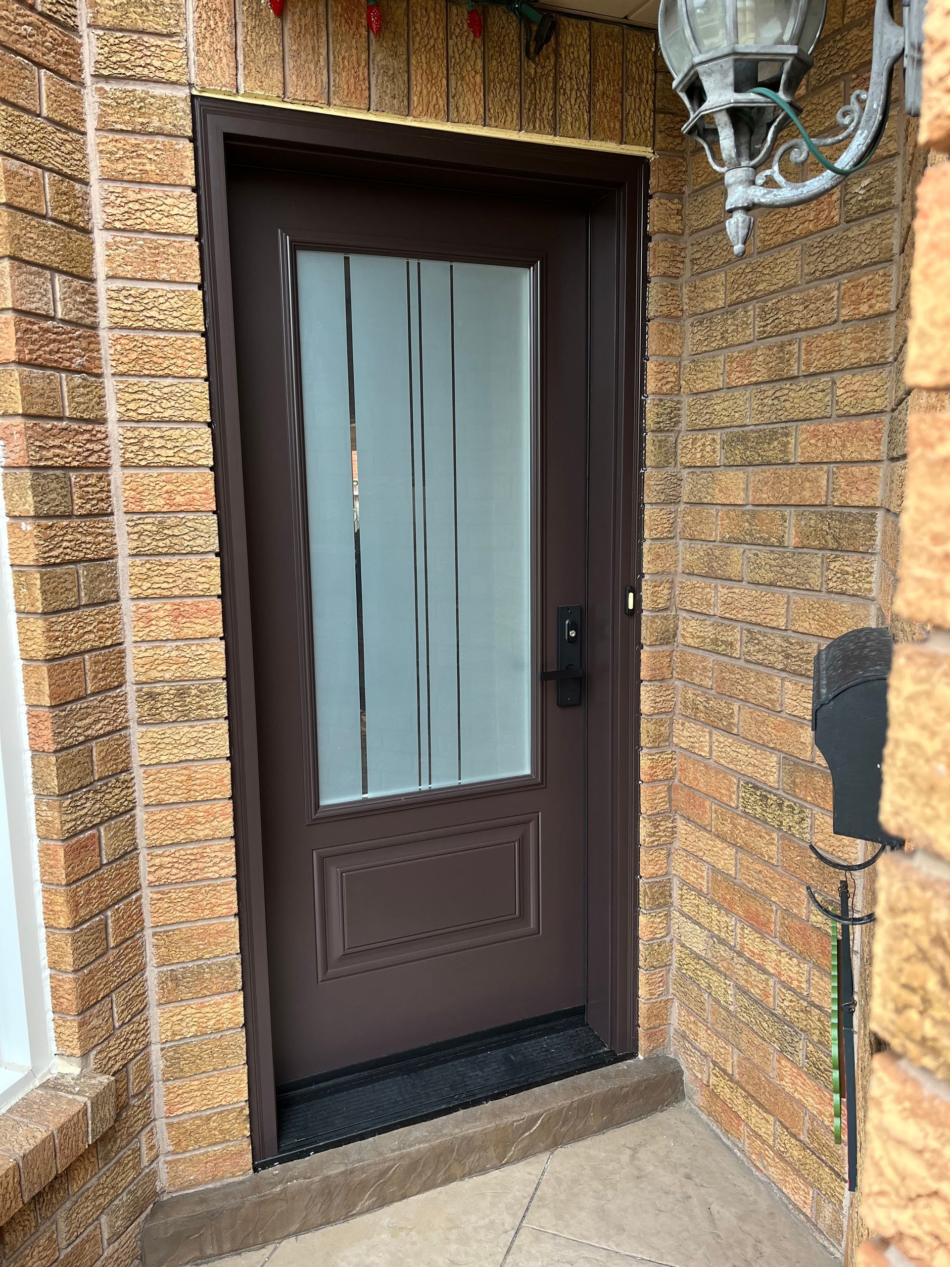 A brown door with a glass window is on a brick wall.