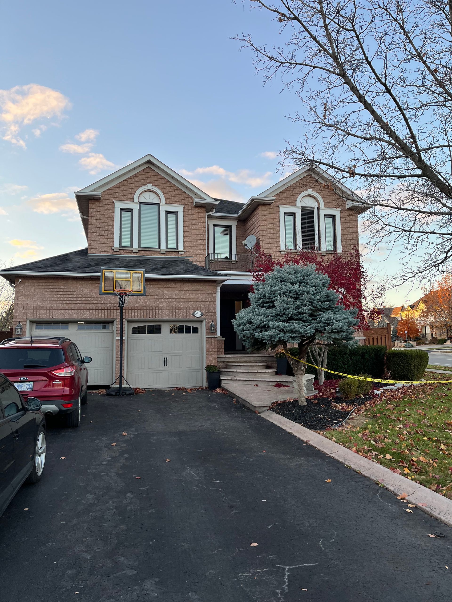 A red car is parked in front of a large brick house.