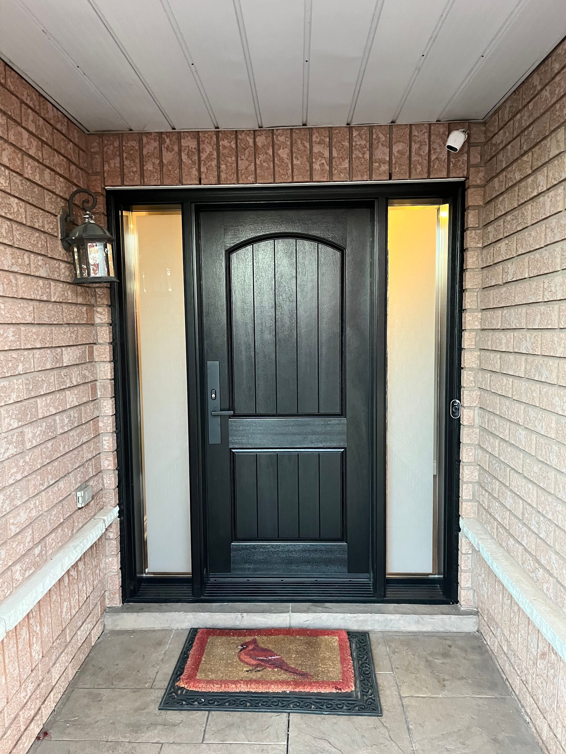 The front door of a brick house with a black door and a rug in front of it.
