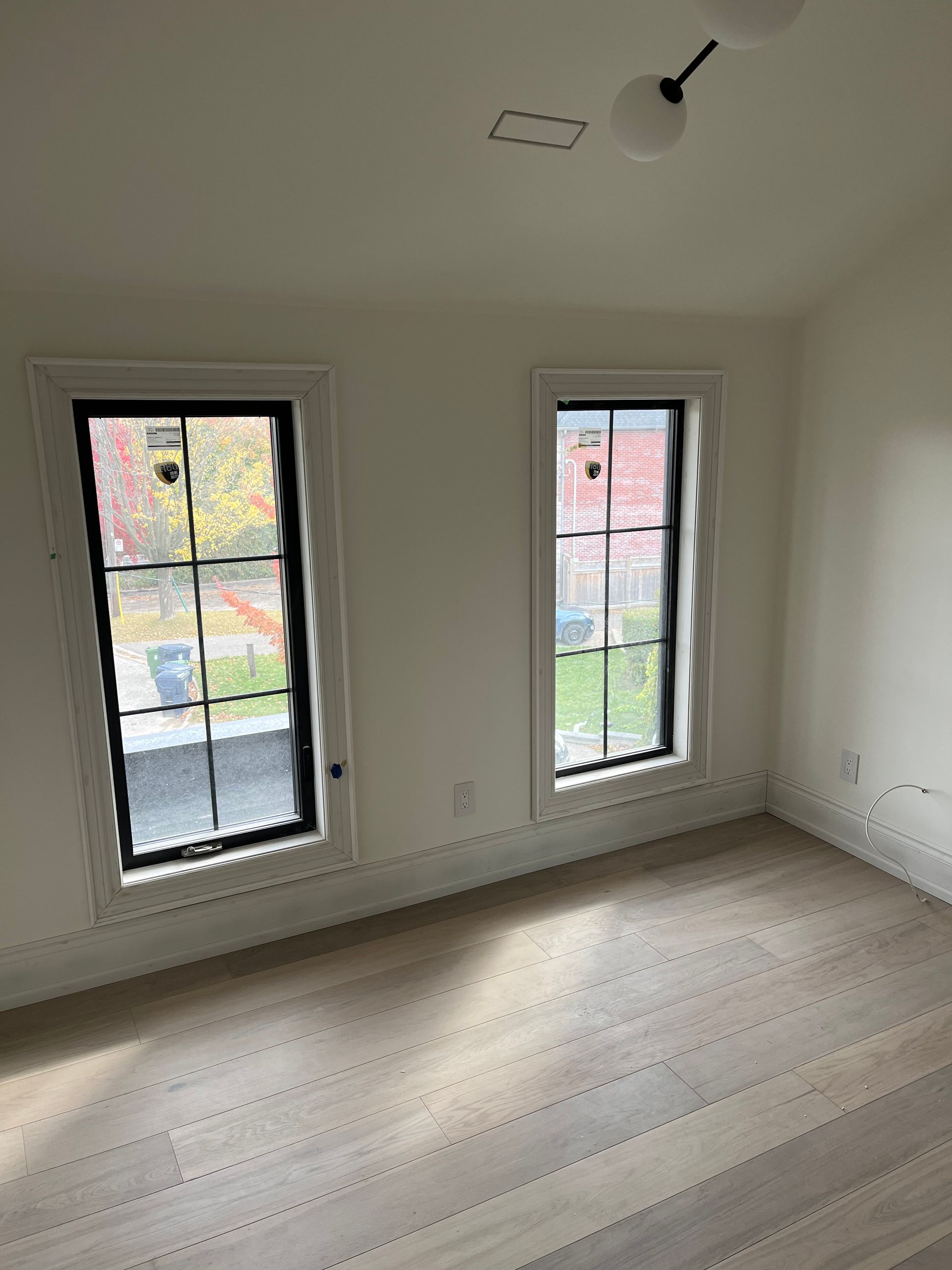 An empty room with two windows and hardwood floors.