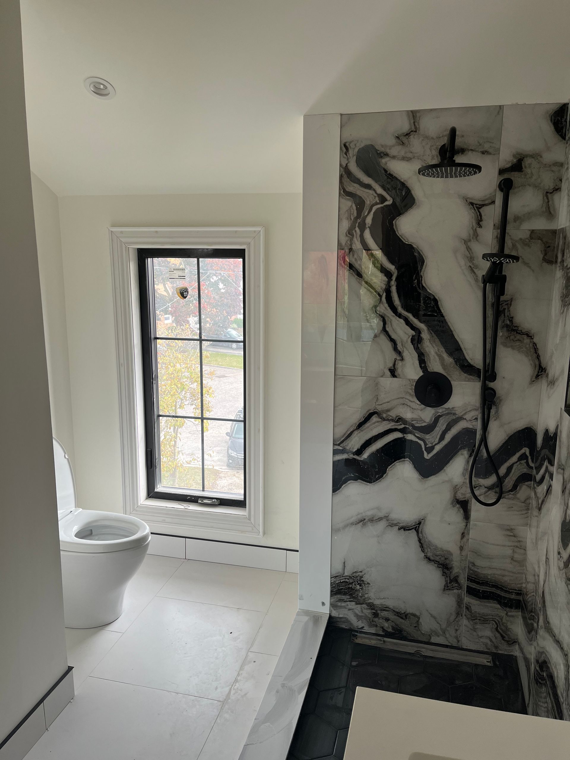 A bathroom with a toilet , shower , and window.