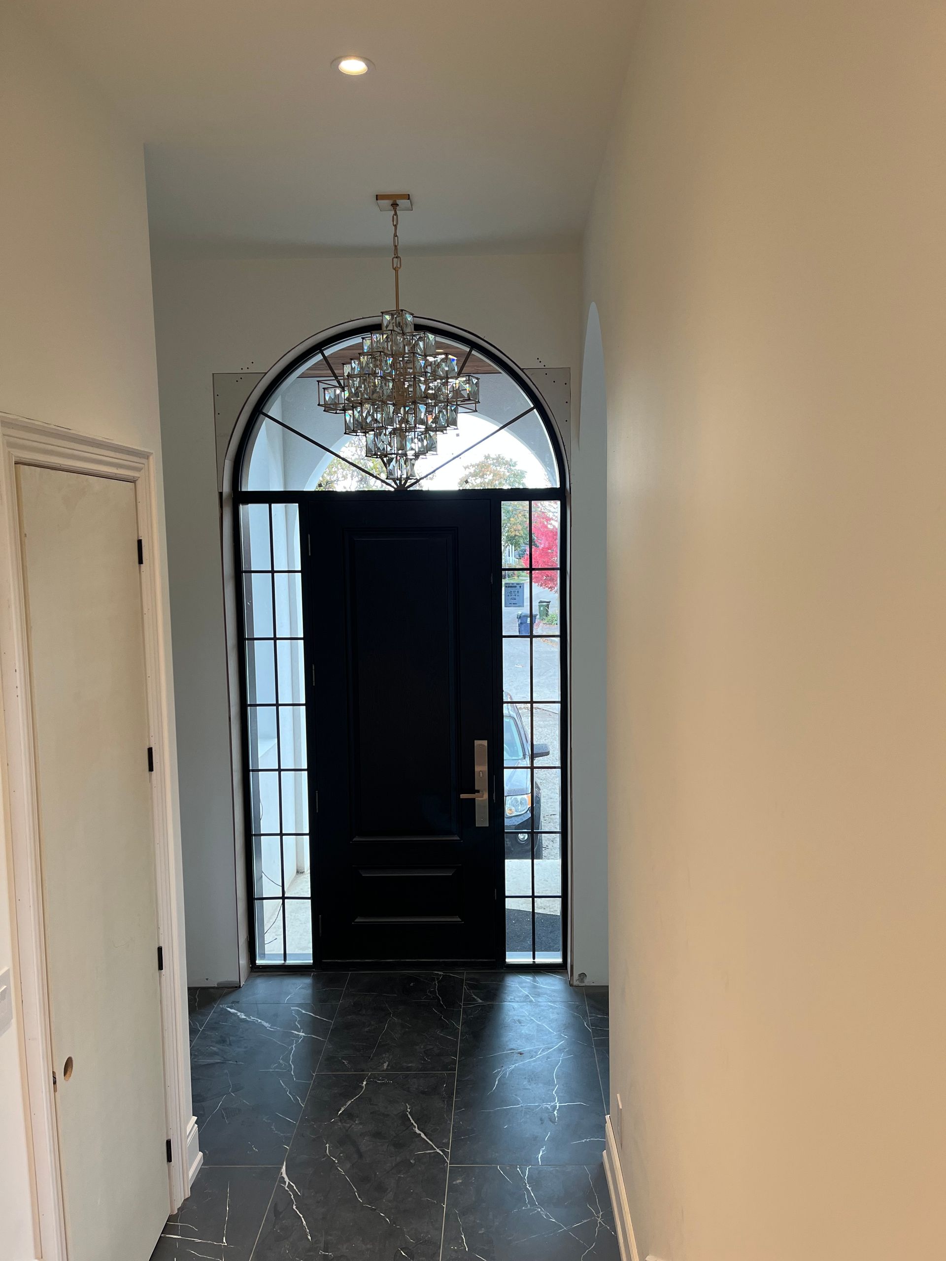 A hallway with a black door and a chandelier hanging from the ceiling.