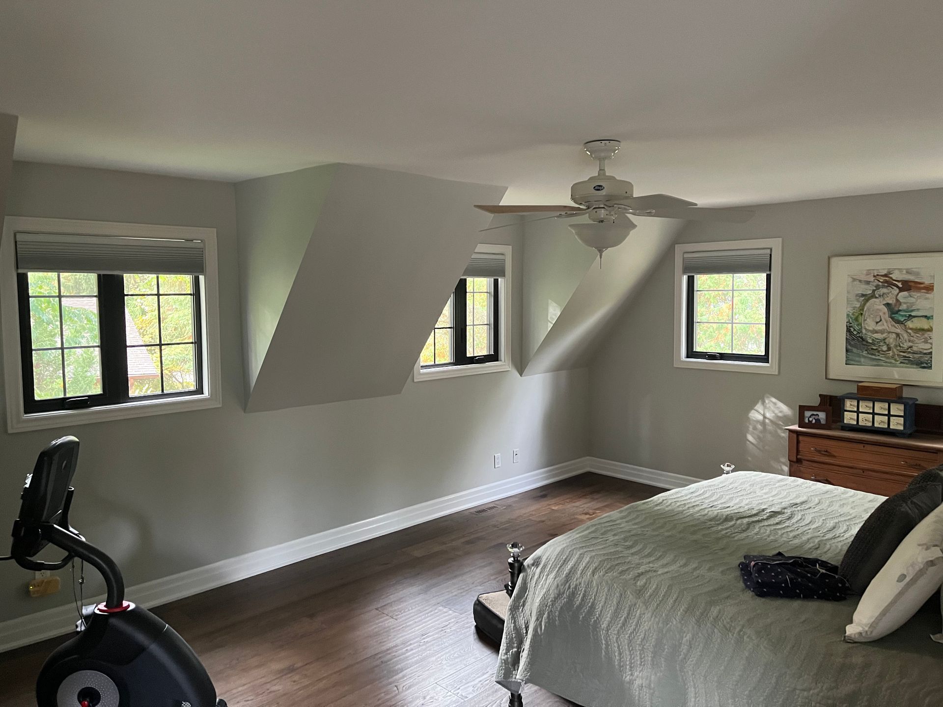 A bedroom with a bed , exercise bike , and ceiling fan.