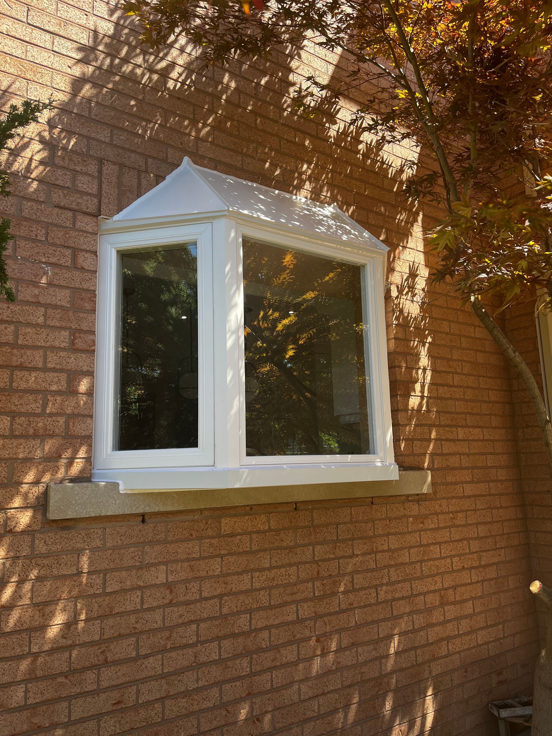 A white window is on a brick wall next to a tree.