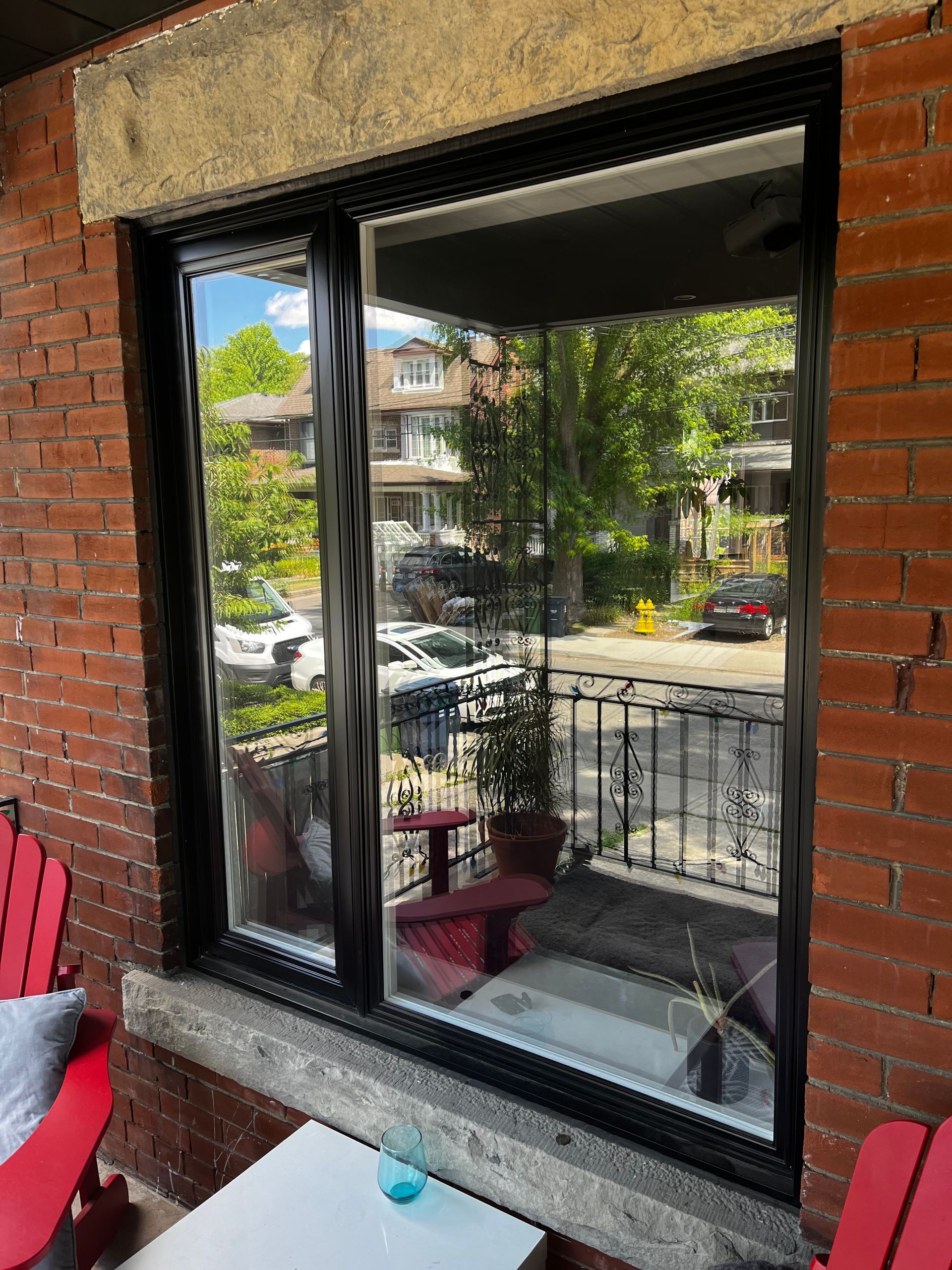 A brick building with a large window and two red chairs on a porch.