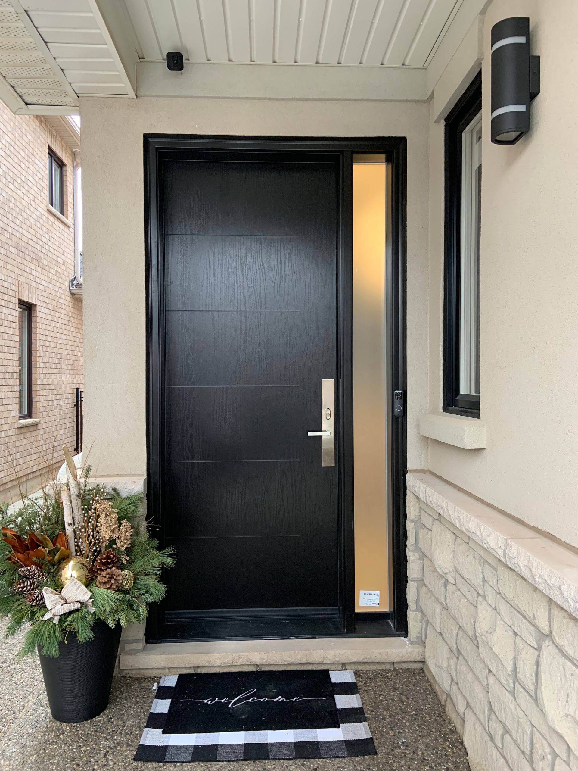 The front door of a house with a black door and a potted plant in front of it.