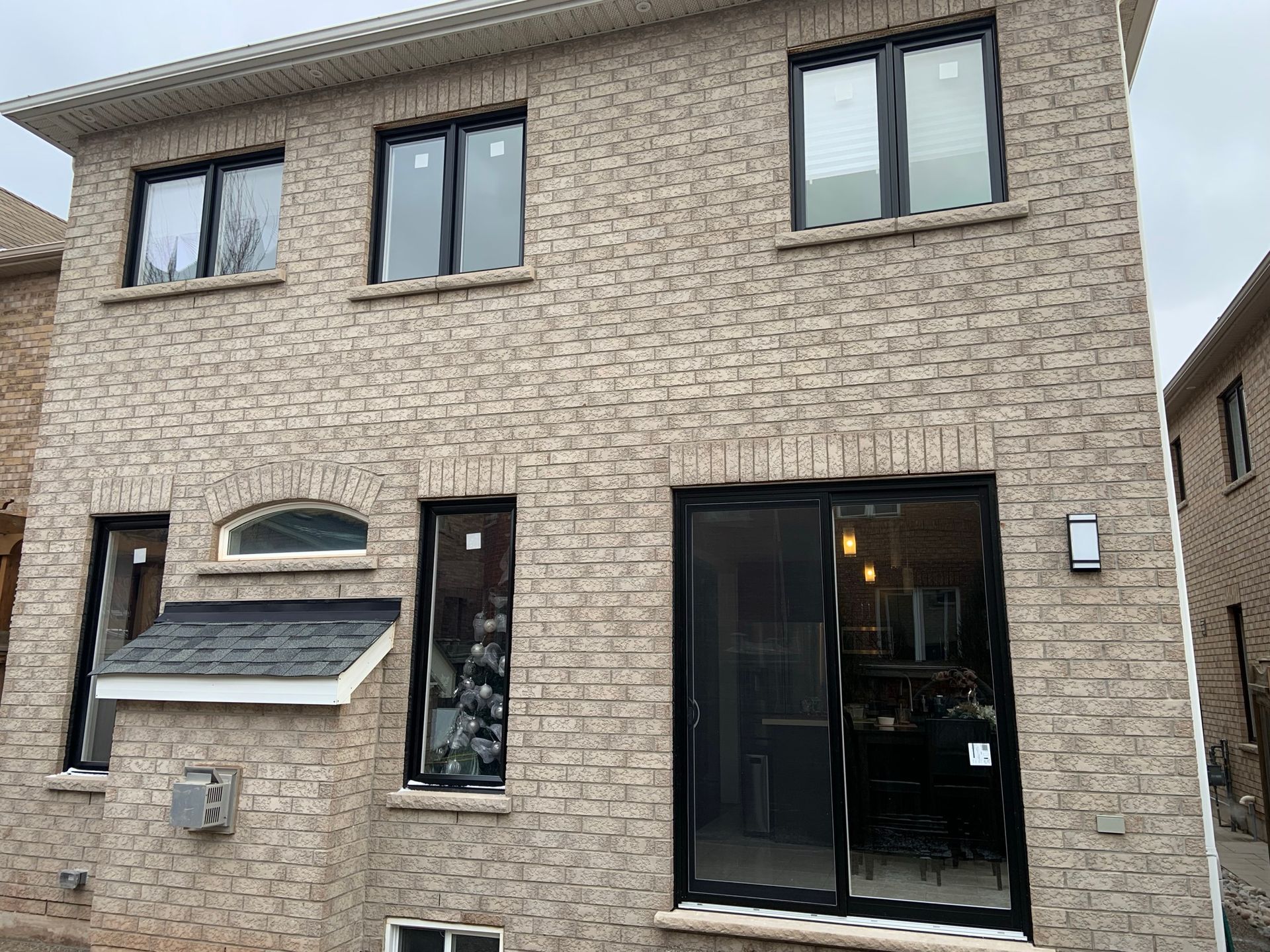 The back of a brick house with black windows and sliding glass doors.