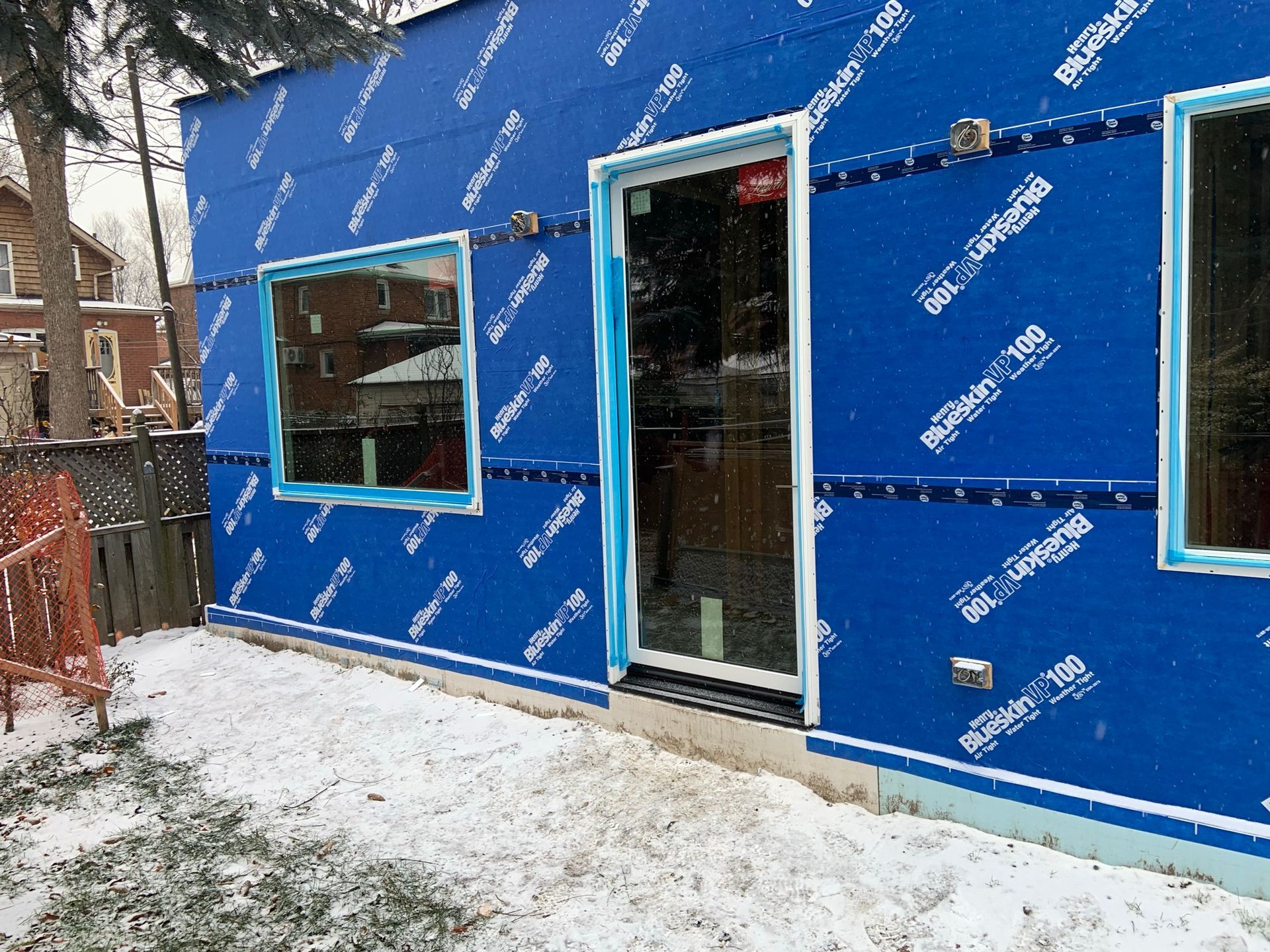 A blue building with a door and windows is covered in snow.