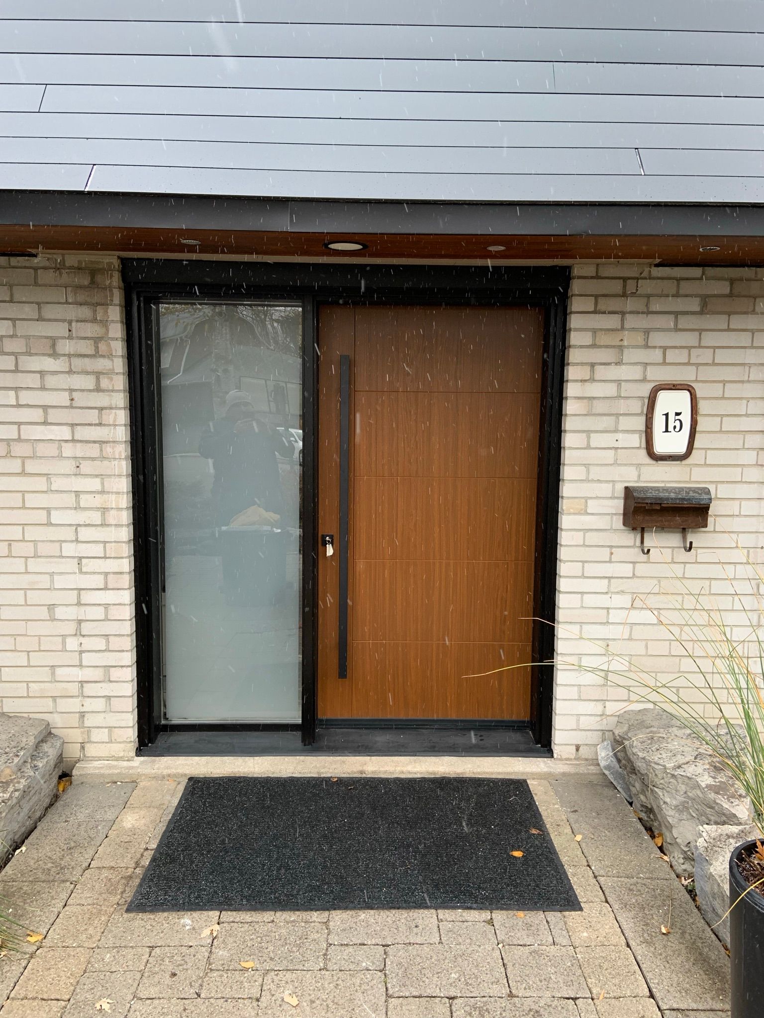 The front door of a brick house with a wooden door and a black mat.