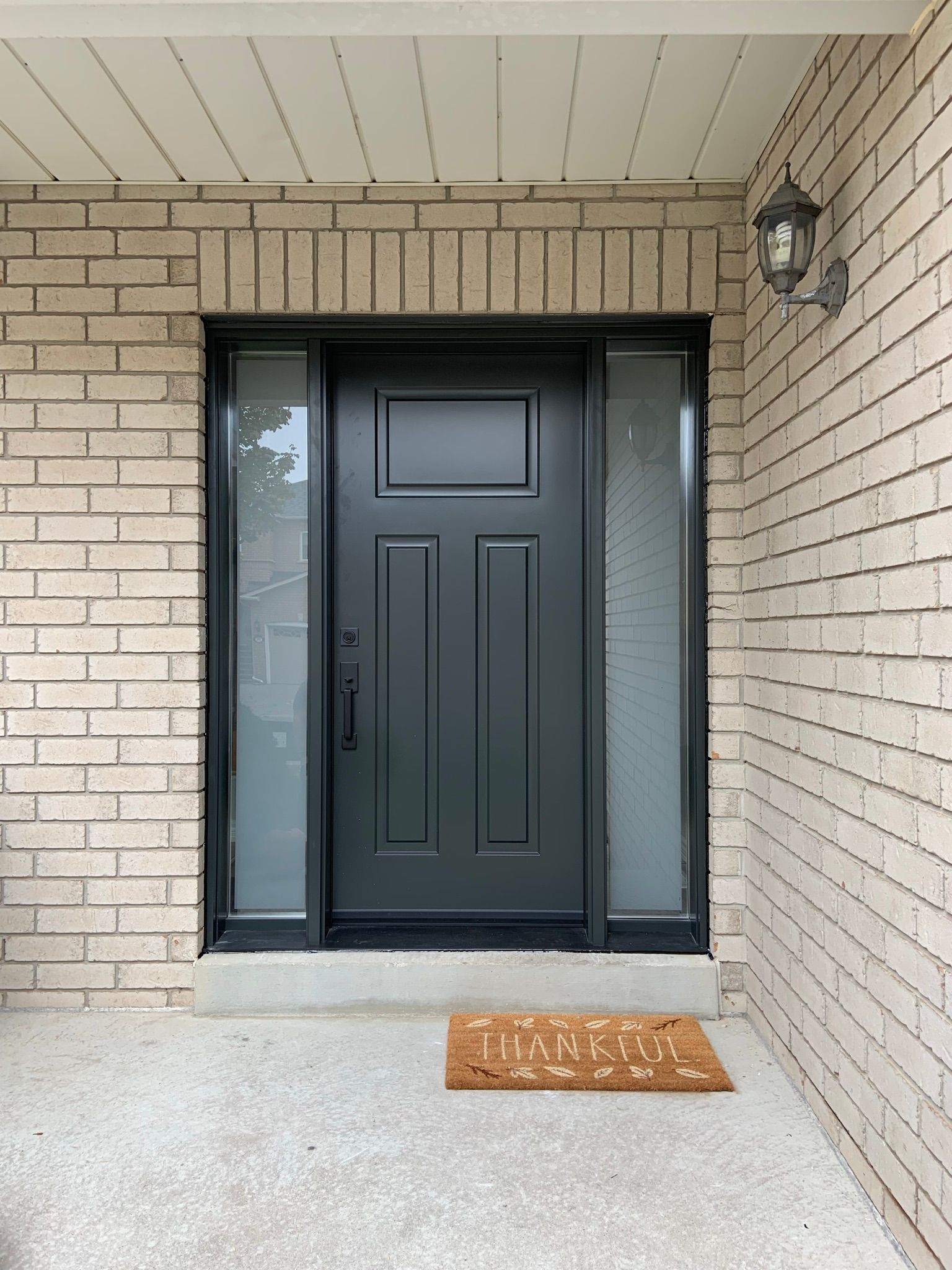 The front door of a brick house with a black door and a welcome mat.