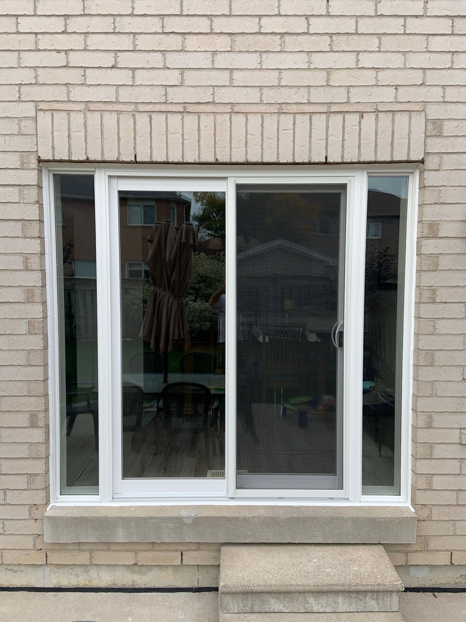 A white sliding glass door is on the side of a brick building.