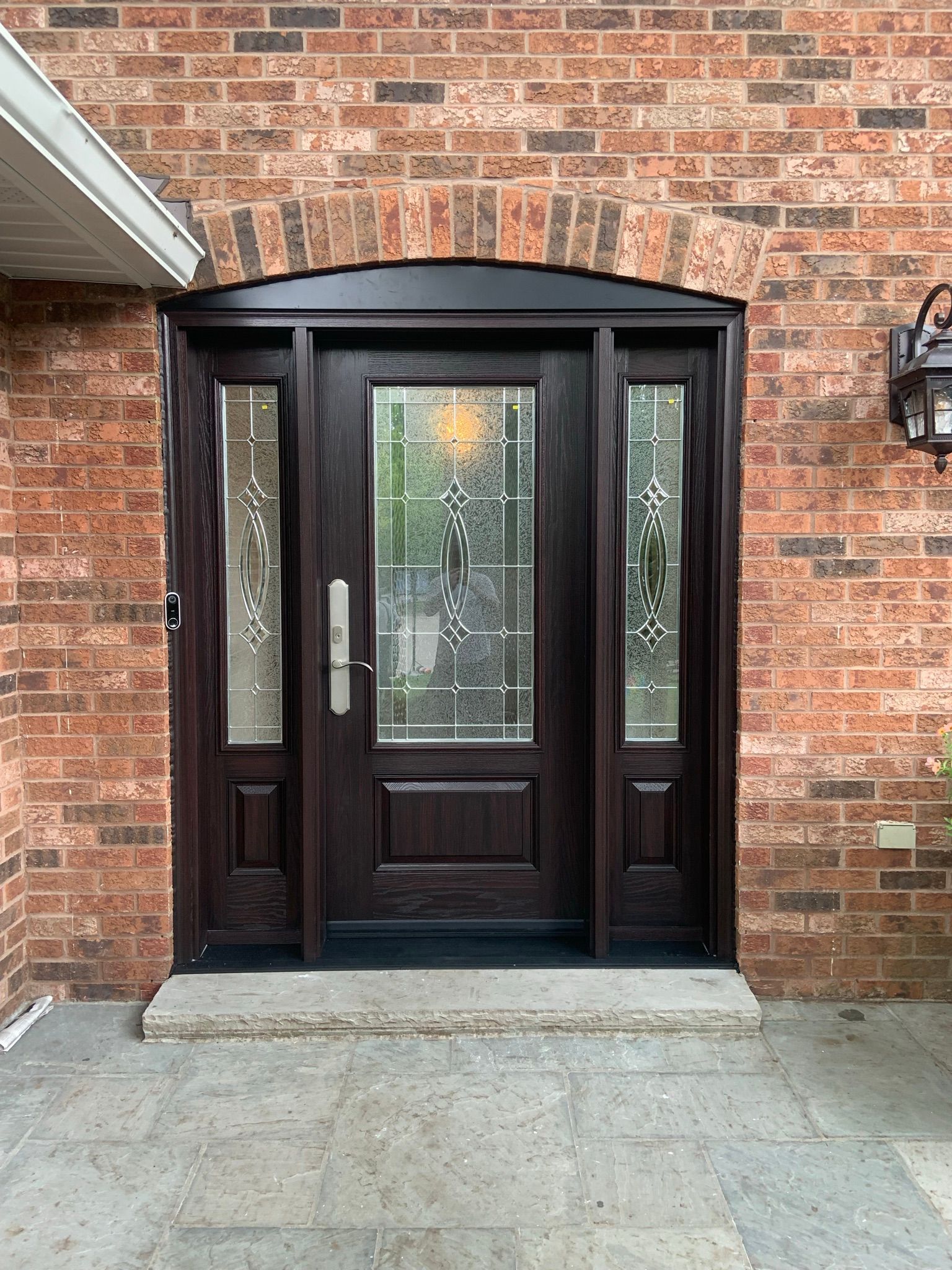 A black front door with a stained glass window is on a brick wall.