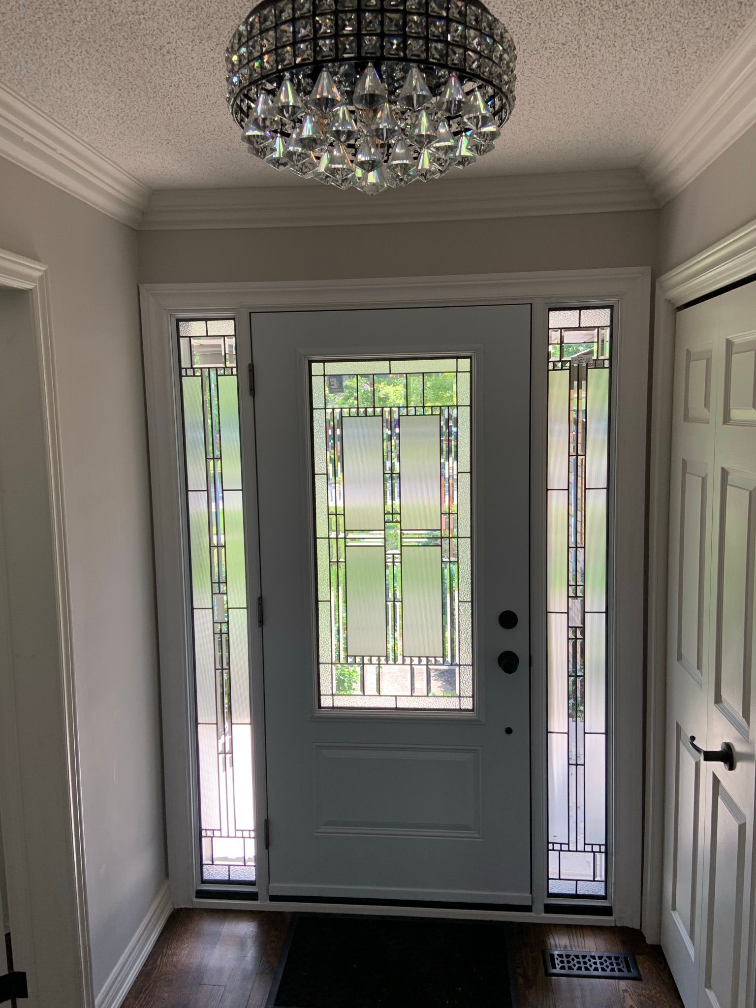 A hallway with a white door and a chandelier hanging from the ceiling.