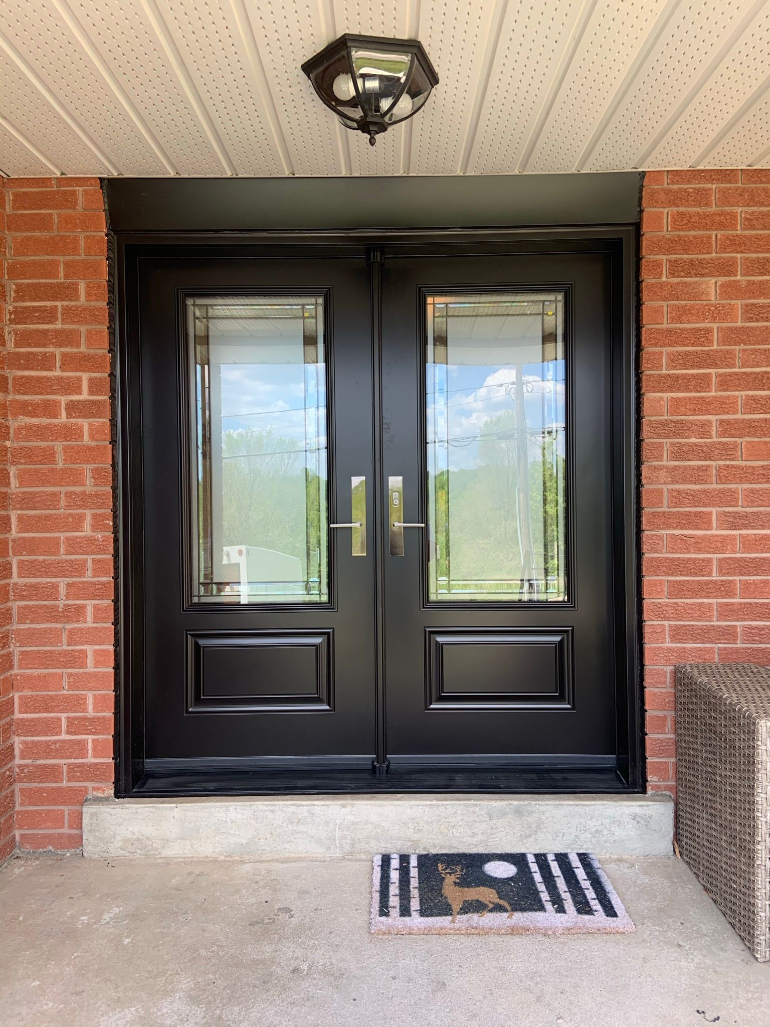 The front door of a brick house with a black door and a welcome mat.