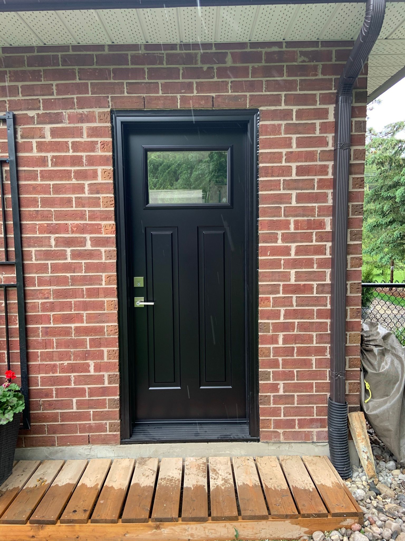 A black door is on a brick wall next to a wooden porch.