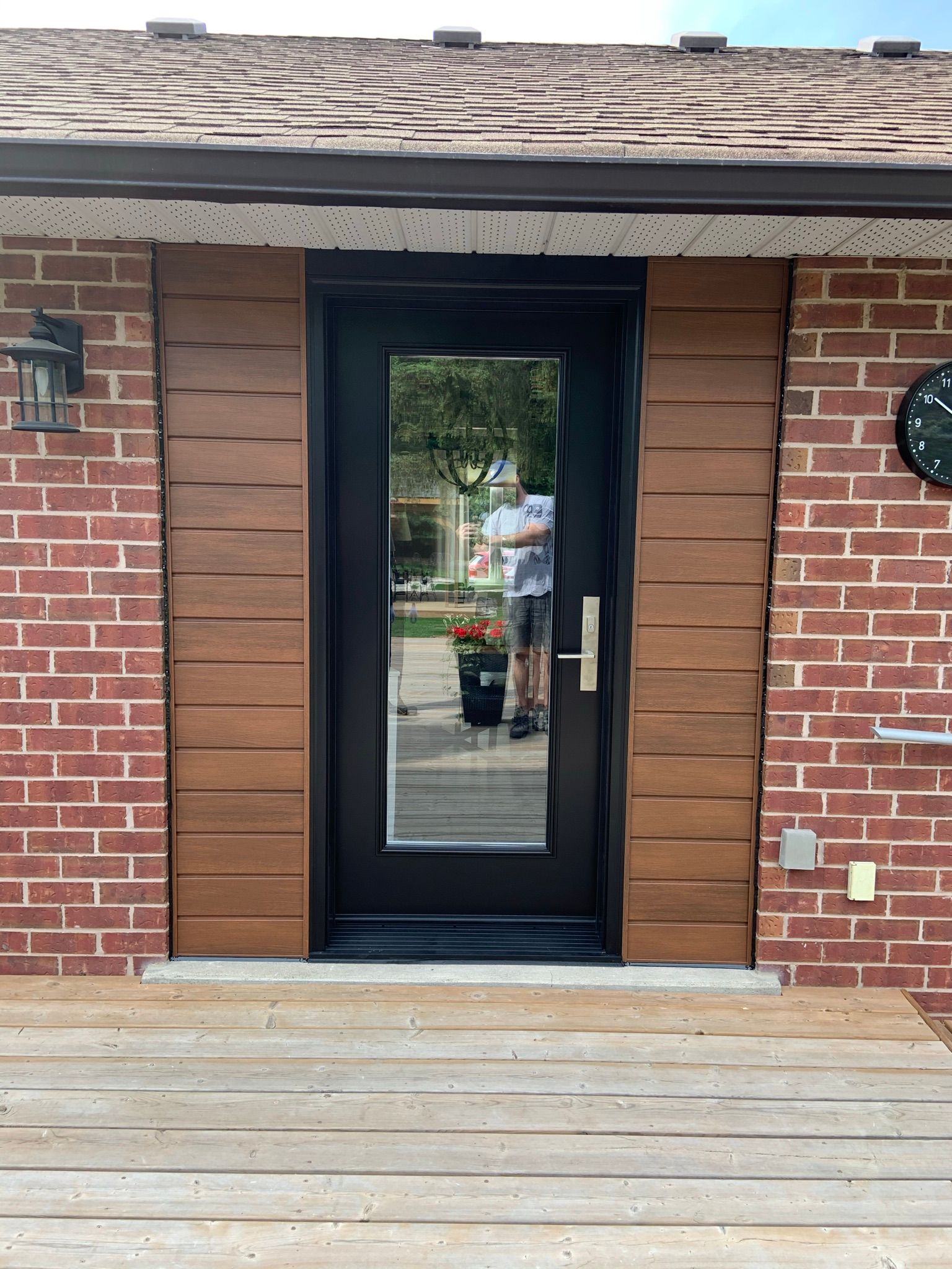 A man is standing in front of a brick house with a black door.