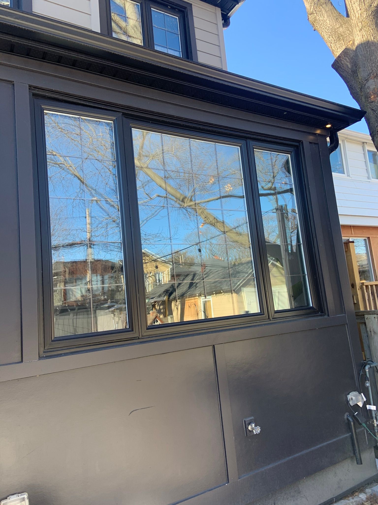 A large window on the side of a house with a tree reflected in it.