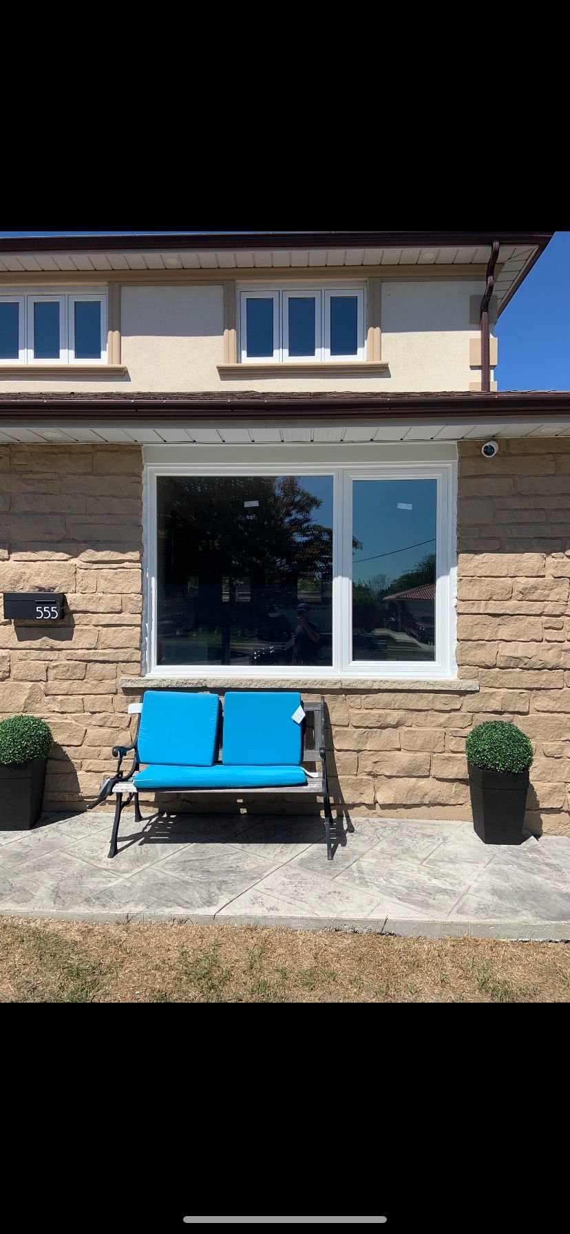A blue bench is sitting in front of a house with a large window.