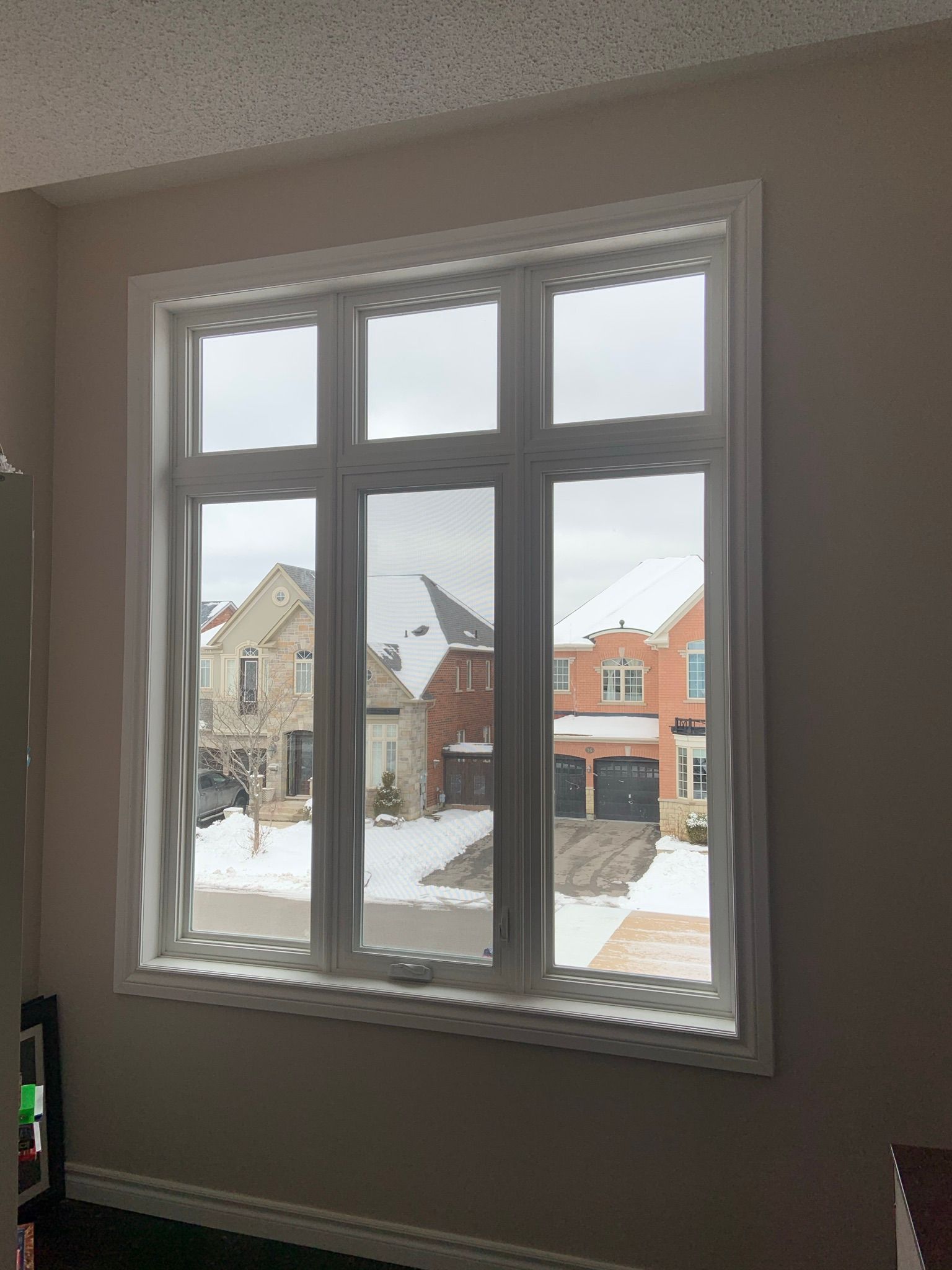 A large window in a living room with a view of a snowy street.