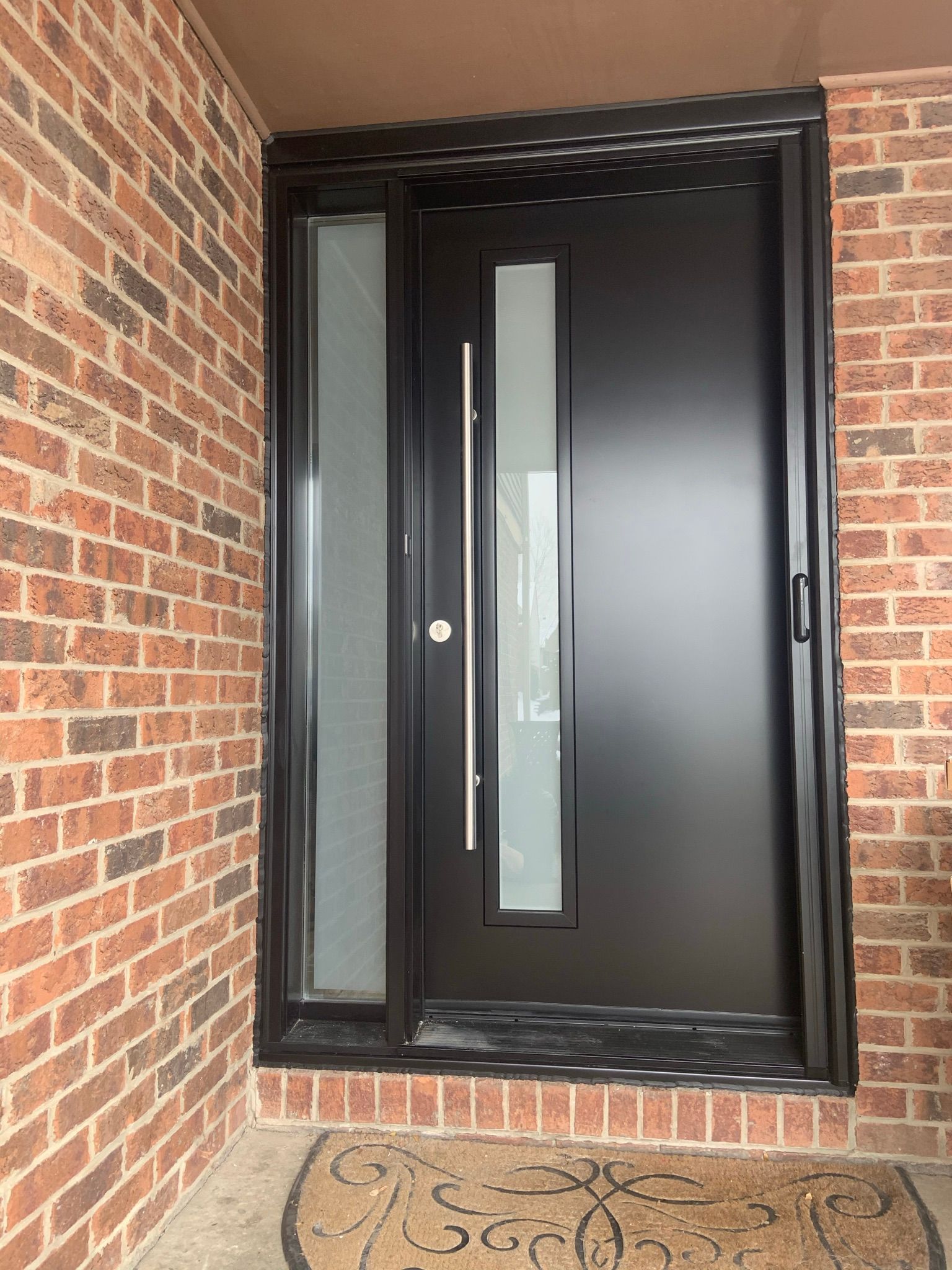 A black door with a glass window is on a brick wall.