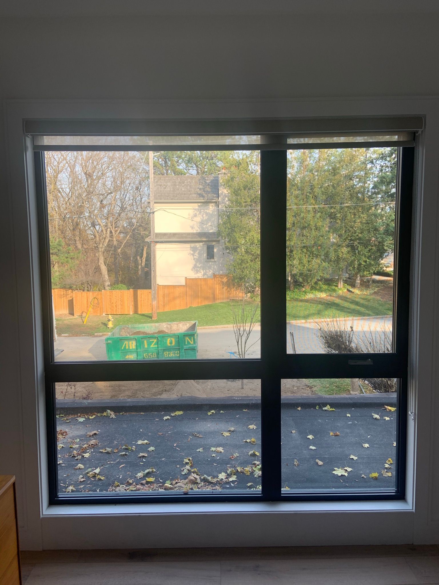 A large window with a view of a house and a green dumpster.