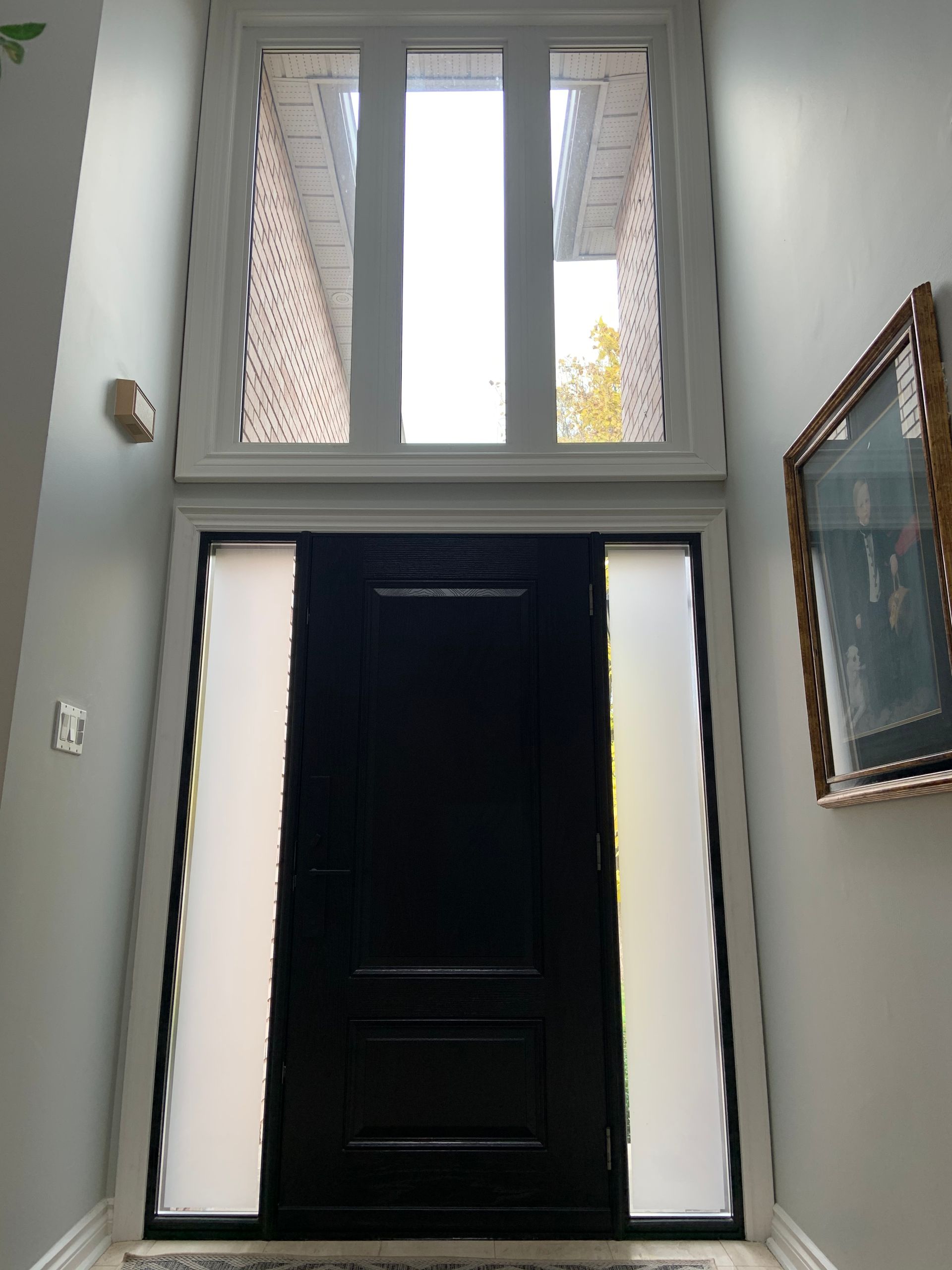 A black door is surrounded by white windows in a hallway.