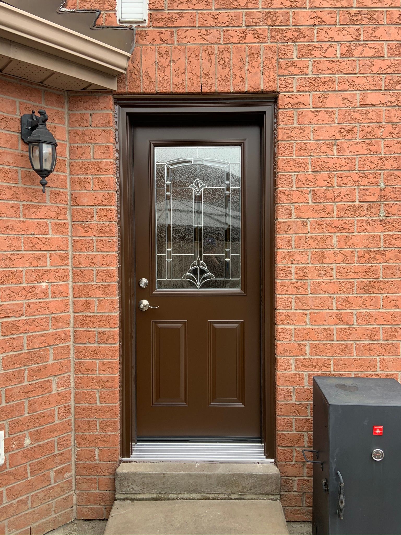 A brown door with a glass window is on a brick wall.