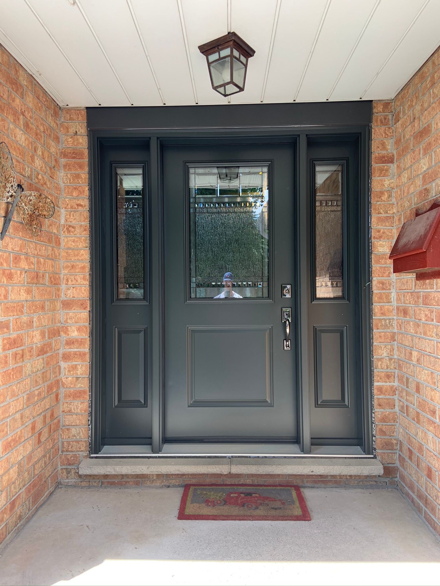 The front door of a brick house with a black door and a lantern hanging from the ceiling.