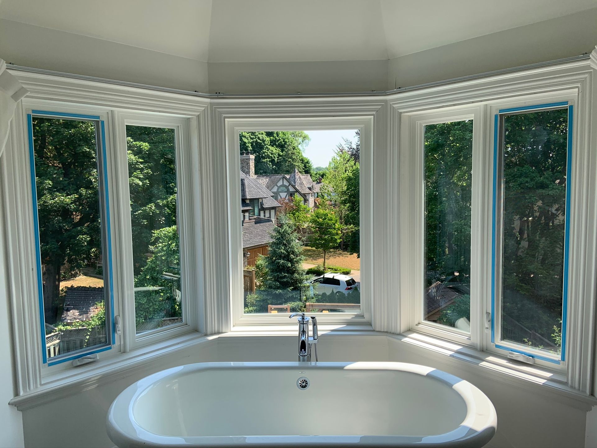 A bathroom with a bathtub and a large window with a view of a house.
