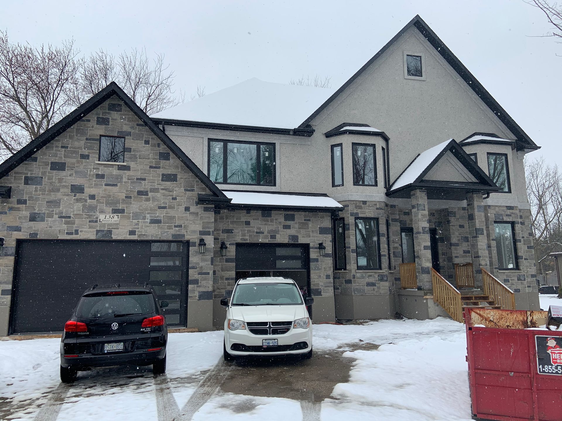 Two cars are parked in front of a large house in the snow.