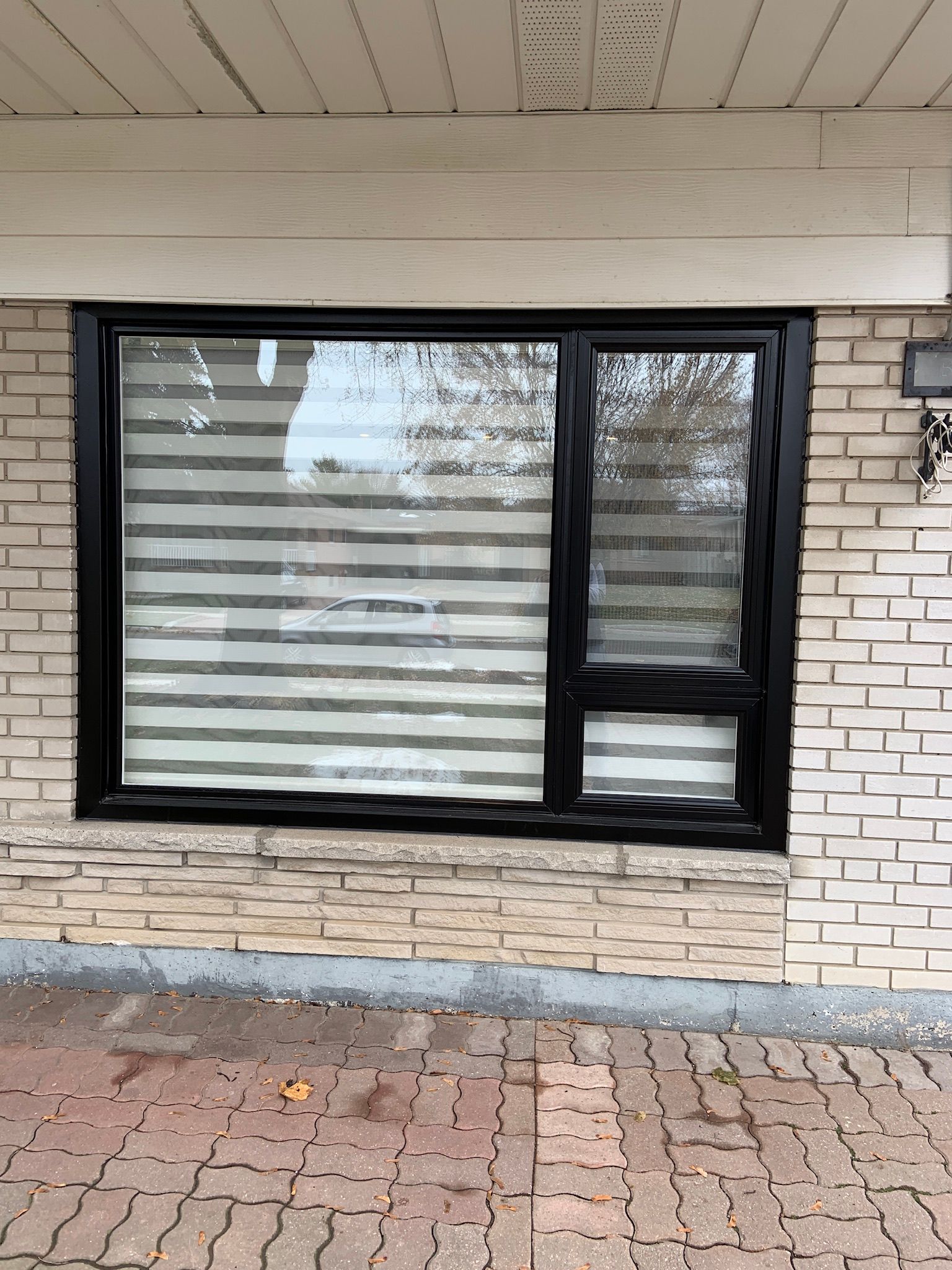 A brick building with a black window and blinds on it.